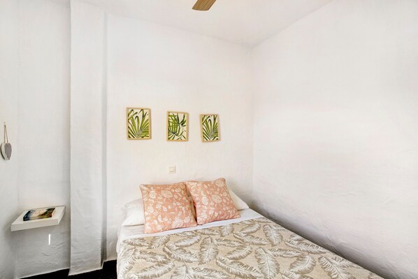 A bedroom with a bed, pillows, a nightstand, a wall-mounted shelf, and three framed pictures. - Vacation Apartment 'Casa Los Caideros' with Sea View, Shared Pool and Wi-Fi (Los Caideros)