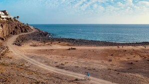 Une route côtière avec un chemin de terre menant à une plage rocheuse, un cycliste et des bâtiments situés sur une falaise.