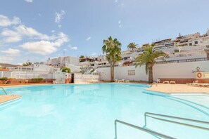 A swimming pool with lounge chairs, palm trees, and buildings in the background.