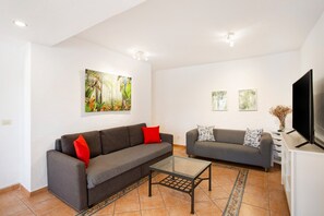 A living room with two sofas, a glass coffee table, a flat-screen TV, and artwork on the walls.