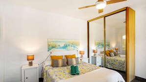 Une chambre d’hôtel avec un lit, des tables de chevet, des lampes, un ventilateur de plafond et un grand miroir.