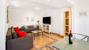 Un salon avec un canapé, une table basse, un téléviseur, une bouteille de vin et un verre.