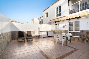 A patio with chairs and a table, a kitchen area, and a stone wall.