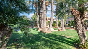Ein gepflegter Garten mit Palmen und Rasen, ein klarer Himmel und ein Gebäude im Hintergrund.