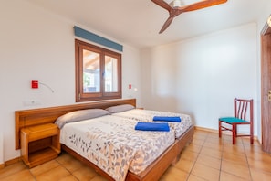 A bedroom with a bed, a wooden nightstand, a chair, a ceiling fan, a window, and a door.