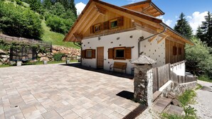 Eine Holzhütte mit Steinverkleidung, einer gepflasterten Terrasse und einem Holzzaun.