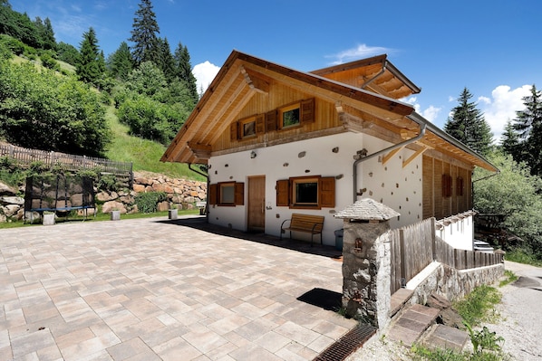 A wooden chalet with a stone facade, a paved patio, and a wooden fence.