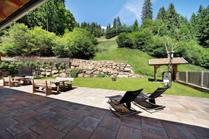 A patio with stone tiles, wooden furniture, and a view of a forested hillside.