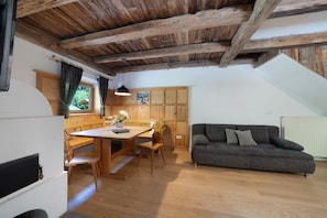 A cozy room with a wooden ceiling, a sofa, a dining table with chairs, and a kitchen area with wooden cabinets.