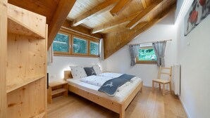 Ein Schlafzimmer mit einem hölzernen Bett, einem Fenster, einem Sessel und einer Heizung.