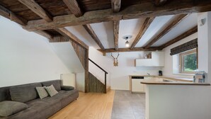 Ein modernes Interieur mit freiliegenden Holzbalken, einer Couch, einer Kücheninsel und einer Treppe.