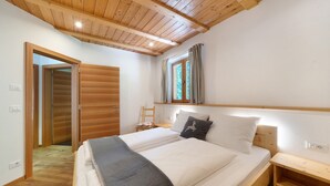 Une chambre avec un plafond en bois, un lit avec une literie blanche, une table de chevet, une fenêtre avec des rideaux et une porte en bois.