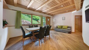 Un coin repas avec un plafond en bois, une table entourée de chaises, un canapé et un téléviseur fixé au mur.