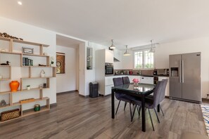 A modern kitchen with a dining area, built-in shelves, and a large refrigerator.