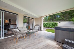 An outdoor patio with wicker furniture, a hot tub, and a grill.
