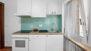 Eine Küche mit weißen Schränken, einer grün gefliesten Spritzschutzleiste, einer Holz Arbeitsplatte, einem Spülbecken und einem Fenster mit Vorhängen.