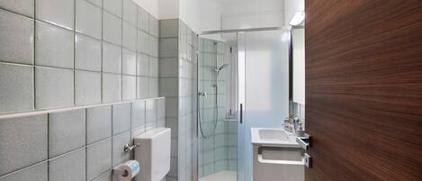 Un baño con ducha, inodoro, lavabo y pared de paneles de madera.