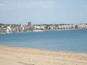 Un paisaje urbano costero con edificios a lo largo de la orilla, una playa arenosa y un mar azul cristalino.