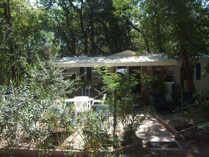 A house surrounded by dense trees, with a covered outdoor seating area and a visible staircase leading to the entrance. - Mobile Home 'Topaze' with Shared Pool, Wi-Fi and Air Conditioning (Puget-sur-Argens)