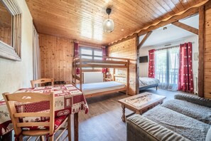 En stuga byggd av trä med våningssängar, ett matbord med en röd- och vitrutig duk, en soffa och en hängande lampa.