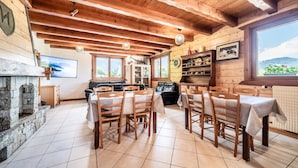 A rustic wooden interior with a dining area, stone fireplace, and a view of the outdoors.