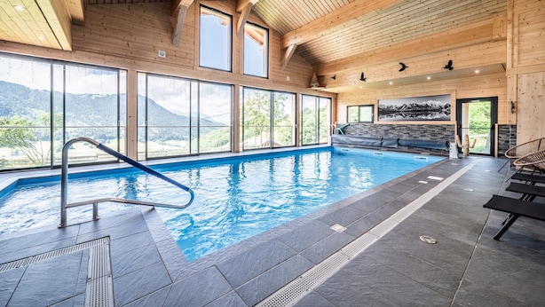 A wooden interior with a swimming pool, large windows, and a view of mountains.