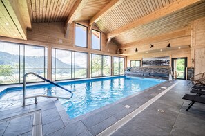 En interiör med träinredning, en swimmingpool, stora fönster och utsikt över bergen.