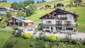 A chalet-style hotel with a balcony, outdoor seating, and a view of the surrounding hillside.