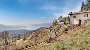 A hillside property with a road leading to a house, surrounded by trees and a view of distant mountains. - Bella Vista Apartment in Premeno with Lake Maggiore View (Premeno)