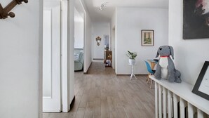 A hallway with a wooden floor, white walls, a small table with a plant, a framed picture, and a gray dog statue. - Bella Vista Apartment in Premeno with Lake Maggiore View (Premeno)