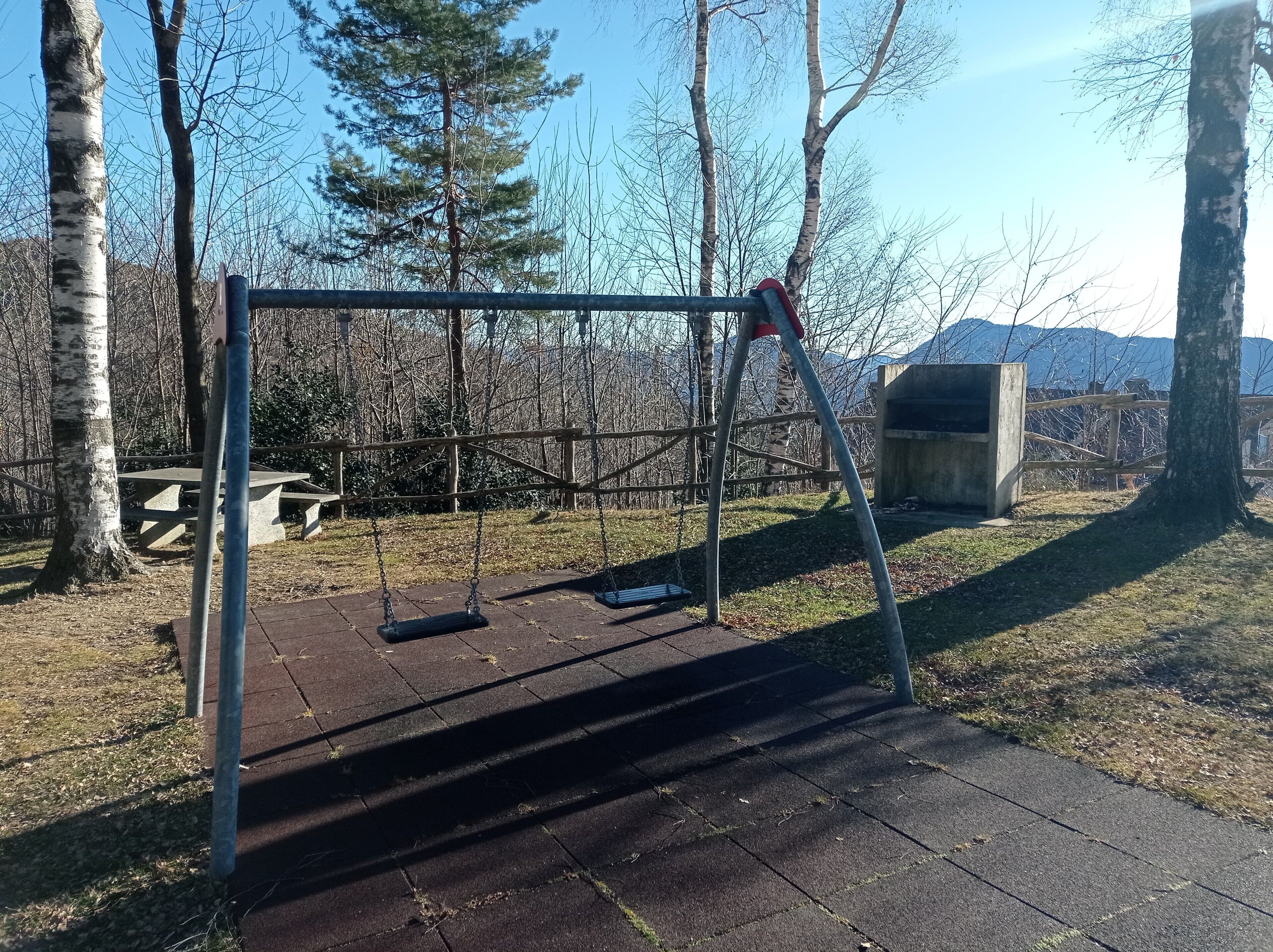 A swing set in a park with a picnic table and a concrete structure in the background.