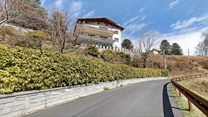 A multi-story building with a stone retaining wall, a curved road, and a guardrail. - Bella Vista Apartment in Premeno with Lake Maggiore View (Premeno)