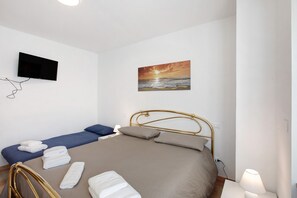 Ein Schlafzimmer mit einem Bett, einem an der Wand montierten Fernseher, einem Sonnenuntergangsbild und einer Nachttischlampe.