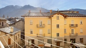 Un edifici de diversos pisos amb balcons, una porta de fusta i vista a muntanyes nevades.