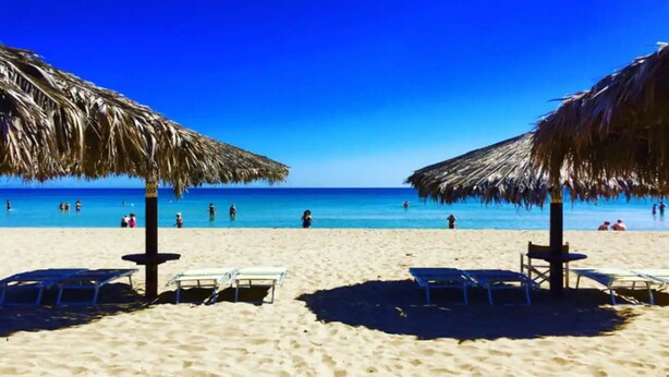 Una playa con sombrillas de paja, sillas de descanso y un mar azul cristalino.