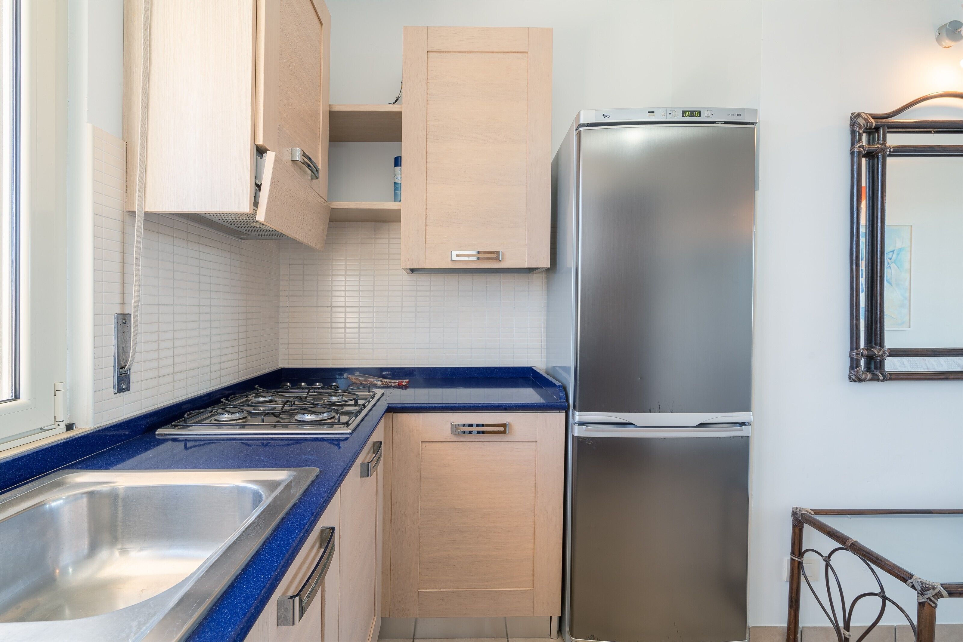 A kitchen with a stainless steel refrigerator, a sink, and wooden cabinets.
