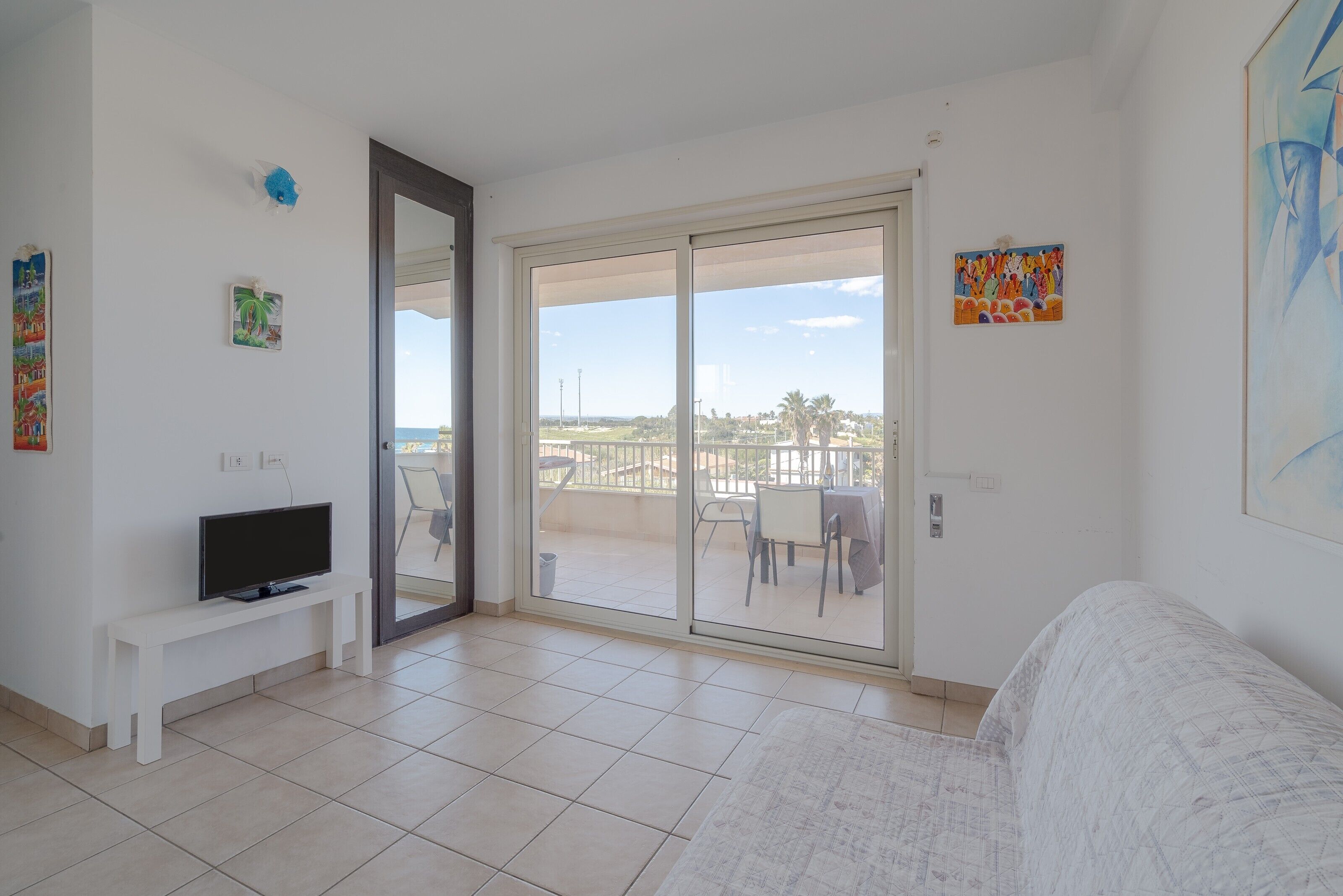 Una sala de estar con televisor, banca, sofá, balcón con vistas y un cuadro.