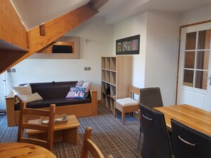 Un espace de vie compact comprenant un canapé, une petite table, une chaise, un bureau en bois et une bibliothèque.