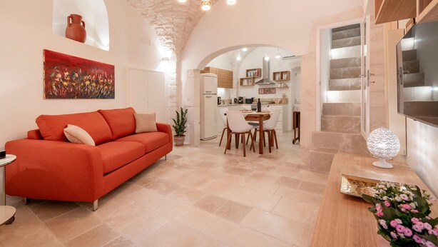 A modern interior with a red sofa, a dining area, kitchen, and a TV mounted on the wall. - Apartment 'Casa Manca' with Private Terrace, Wi-Fi and Air Conditioning (Locorotondo)