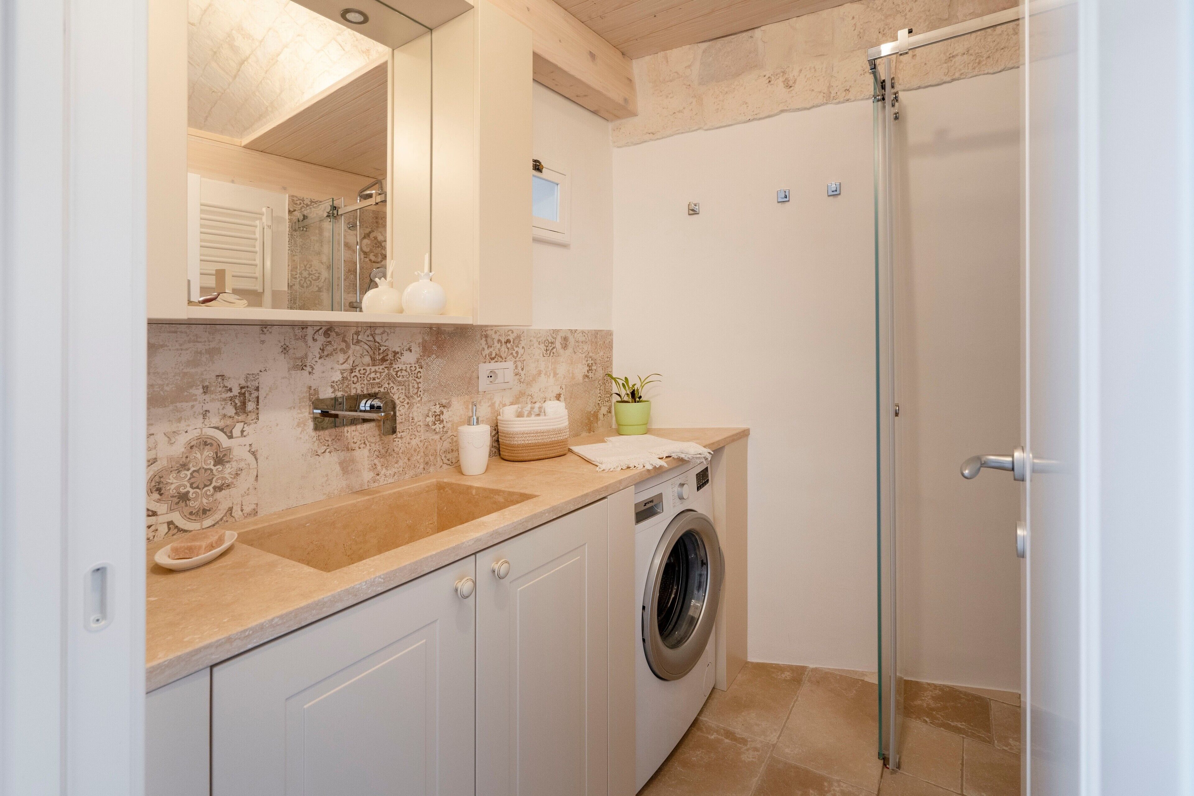 A modern bathroom with a washing machine, a sink, a mirror, and a shower.
