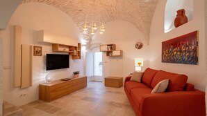 A spacious living area with a stone ceiling, a flat-screen TV, a red sofa, and a painting on the wall. - Apartment 'Casa Manca' with Private Terrace, Wi-Fi and Air Conditioning (Locorotondo)