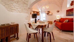 A dining area with a table, chairs, a wooden cart, and a red sofa in the background. - Apartment 'Casa Manca' with Private Terrace, Wi-Fi and Air Conditioning (Locorotondo)