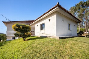 Une maison à deux étages, avec un toit en tuiles, un petit jardin devant et un arbre.
