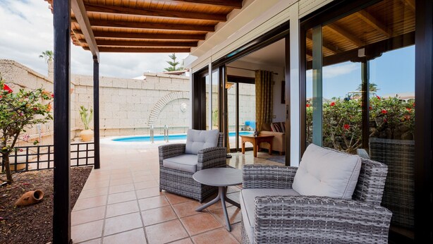 Une terrasse couverte aménagée avec des meubles en osier, une piscine et une vue sur le paysage environnant.