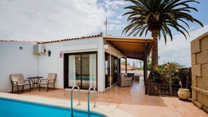 Une piscine avec une terrasse ensoleillée, des sièges extérieurs et un palmier.
