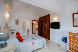 Un dormitorio con cama, lámpara de noche, armario de madera, televisor y espejo.