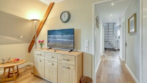 A modern living room with a wooden cabinet, a flat-screen TV, a clock, and a staircase leading to another room. - 3 bedroom gorgeous apartment in List (List)