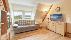A cozy loft bedroom with a gray sofa, wooden dresser, and a large TV on a wooden wall. - 3 bedroom gorgeous apartment in List (List)