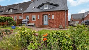 A two-story brick house with a sloped roof, a front porch, and a garden with various plants and flowers. - 3 bedroom gorgeous apartment in List (List)