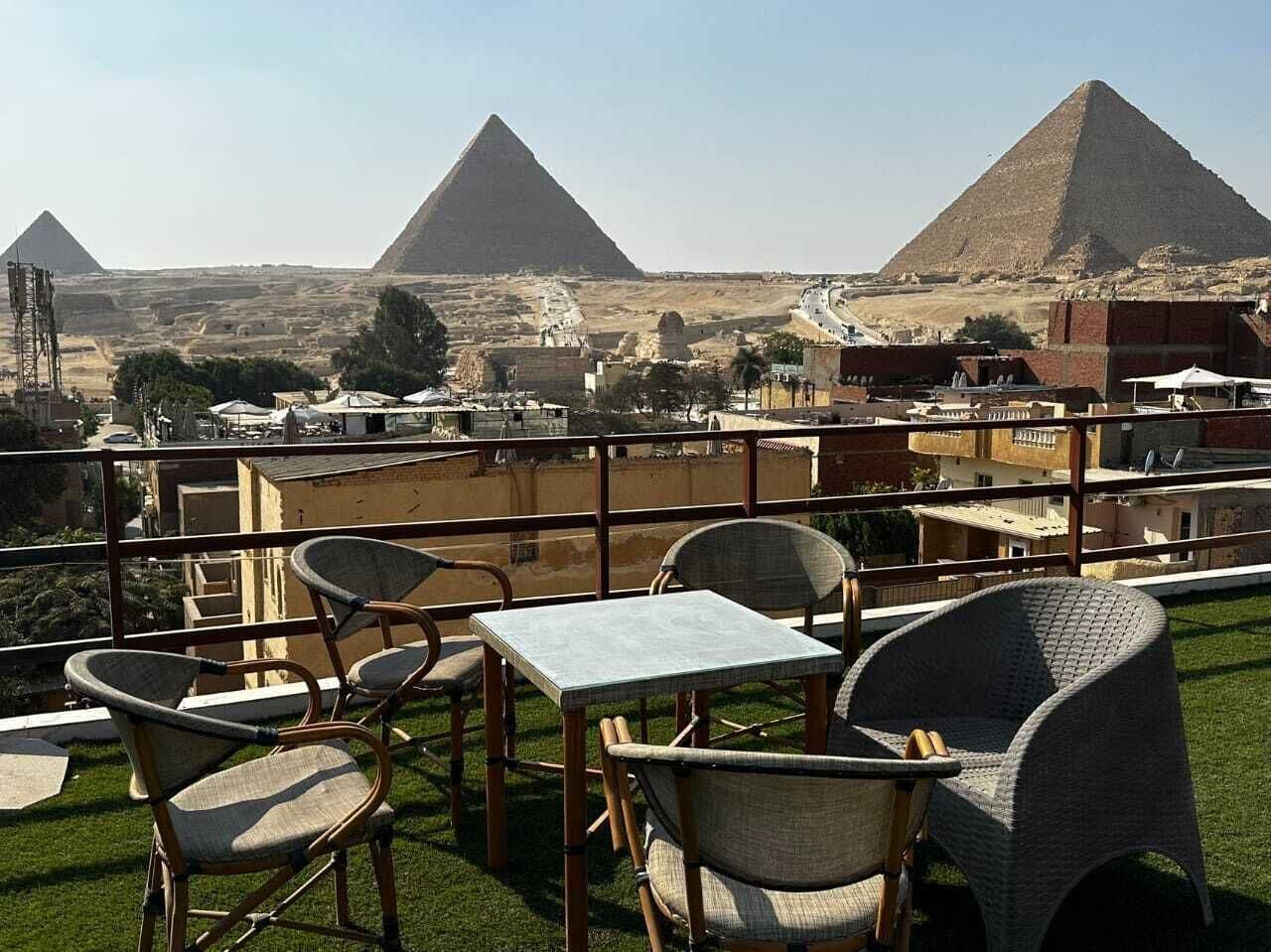 Zona de estar al aire libre con mesas y sillas, con vista a las pirámides.
